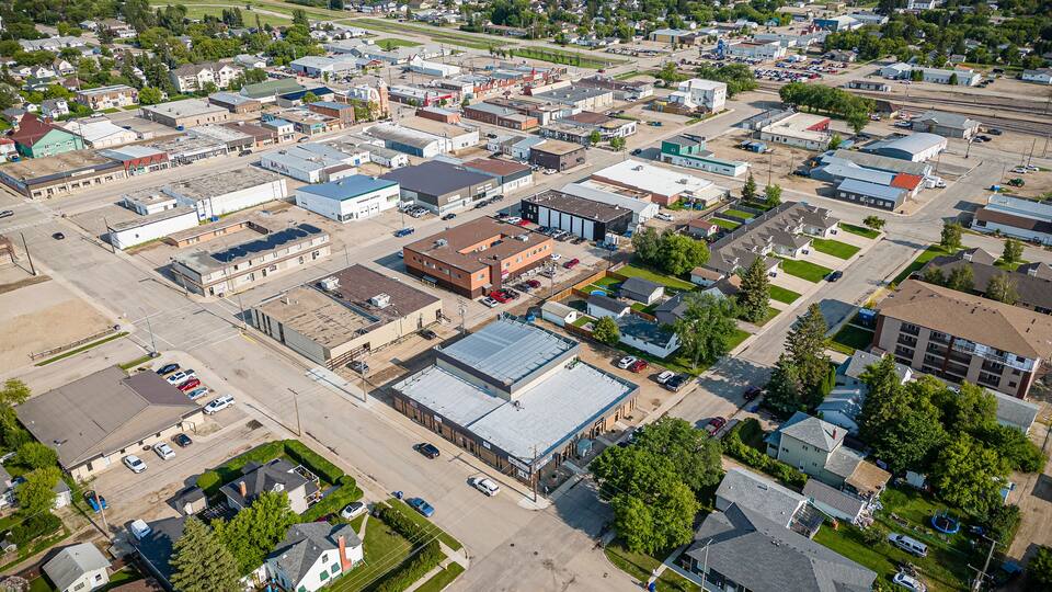 An aerial view of a small town with a mix of residential and commercial buildings, a central road, and surrounding green fields.