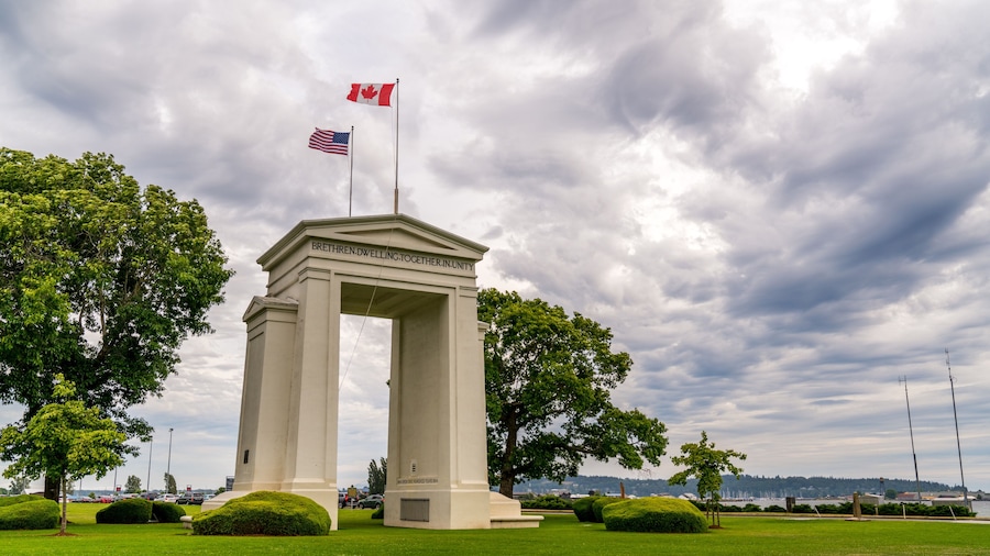 Vancouver-Blaine Hwy, Surrey, British Columbia, Canada - US Peace Arch border crossing. Canadian and US flags are waiving in the wind on a beautiful cloudy sky.
