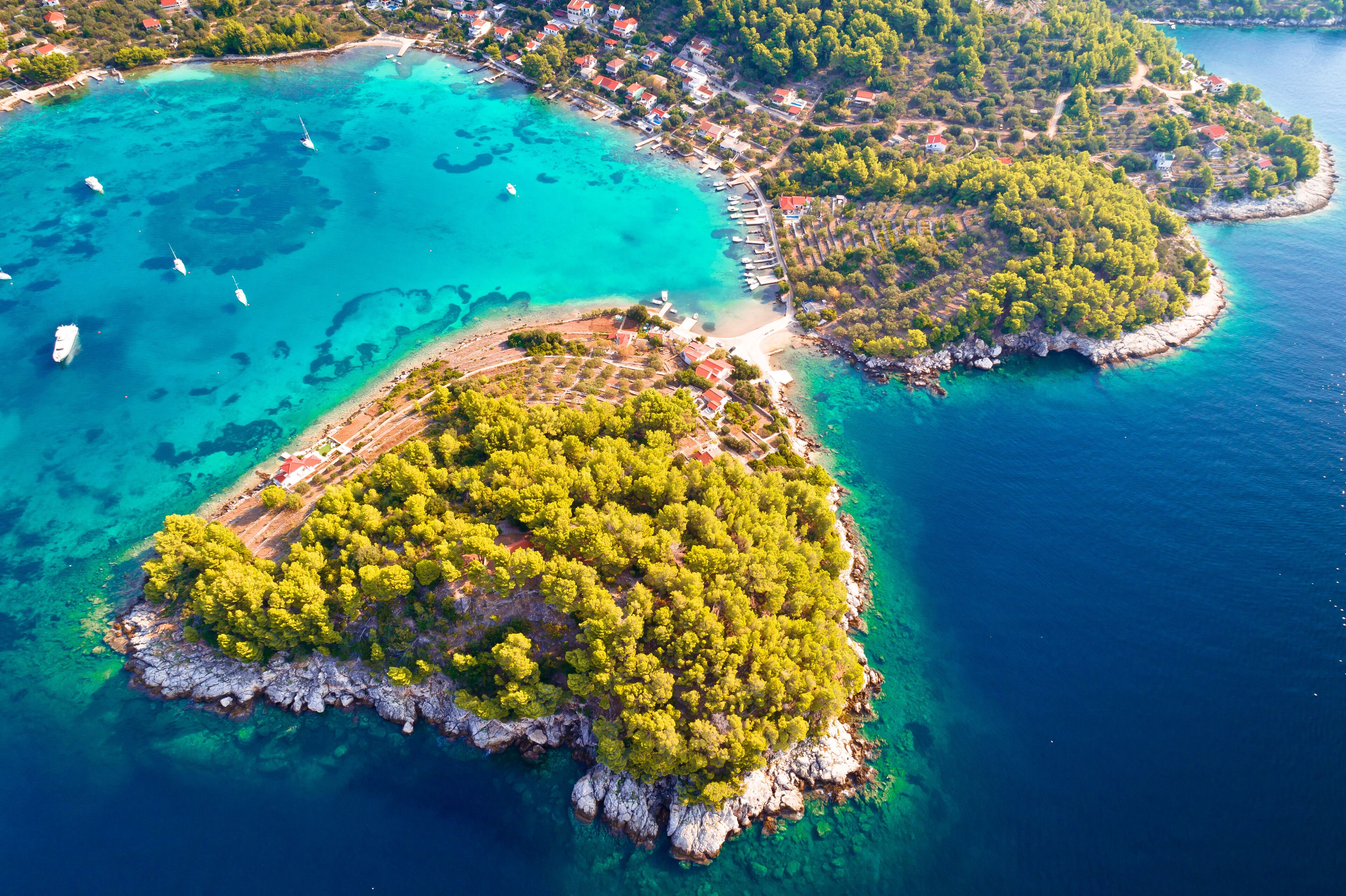 An aerial view of a coastal area with clear turquoise waters, small islands with dense green vegetation, and a few boats anchored near the shore.