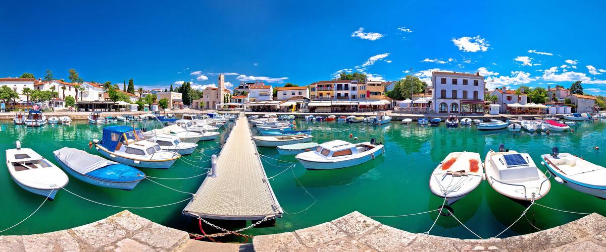 A marina with numerous boats docked, a pier, and a coastal town with buildings.