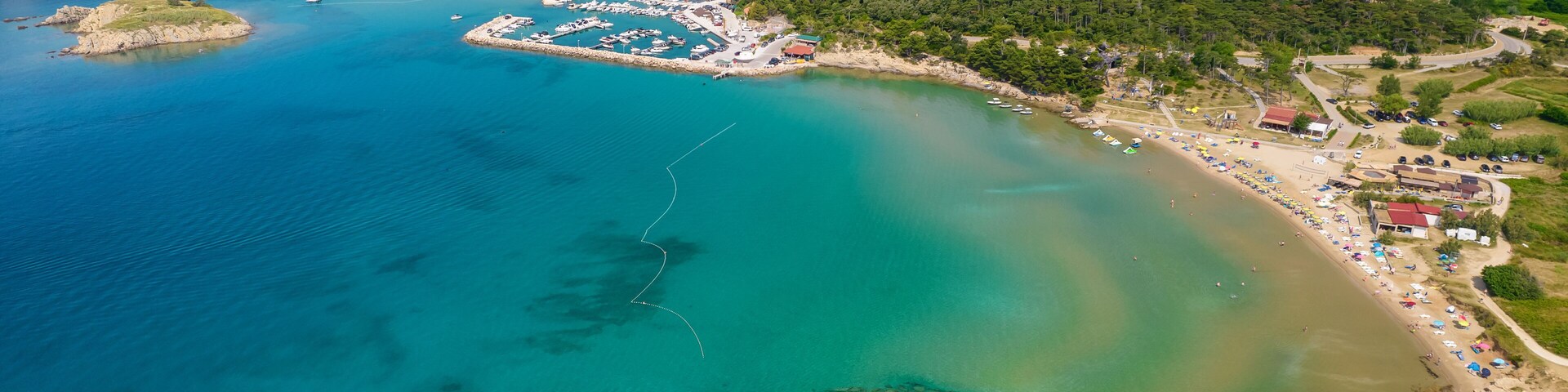 A coastal town with clear turquoise waters, a marina, and a beach with umbrellas.