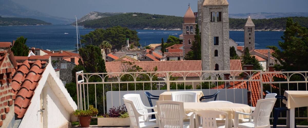 A coastal town with a prominent church tower, terracotta-roofed buildings, and a view of the sea.