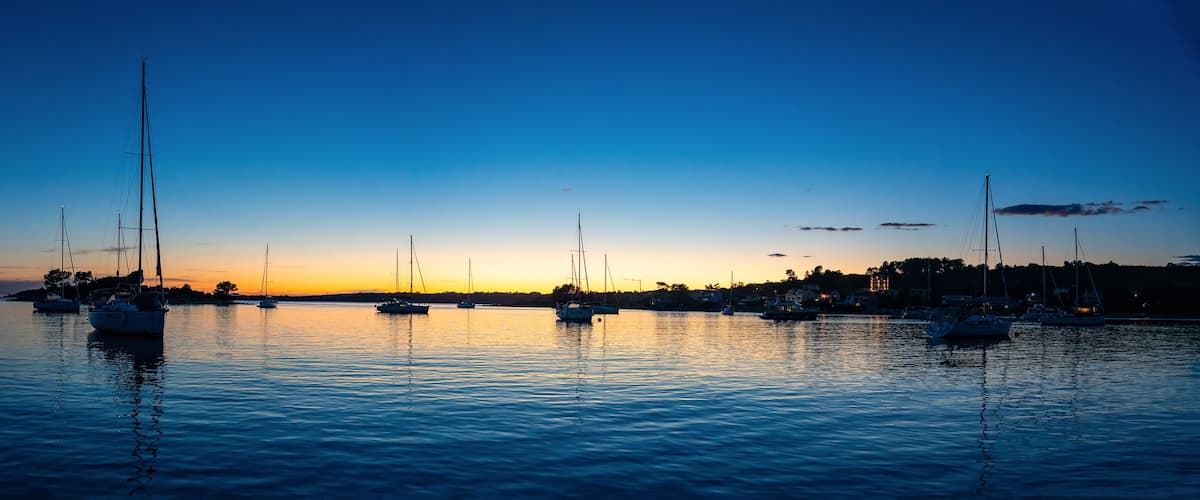 A marina at sunset with several sailboats anchored in calm waters.