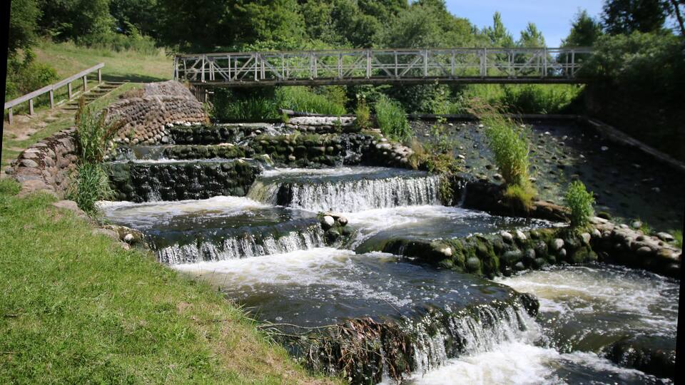 A cascading water feature with a wooden bridge in the background.