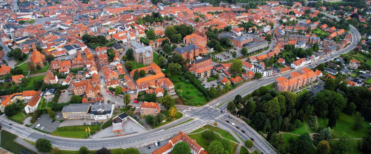 An aerial view of a town with red-roofed houses, green spaces, and a central roundabout.