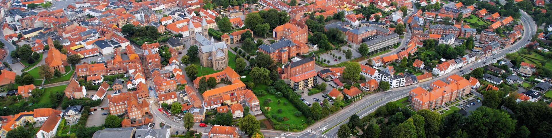 An aerial view of a town with red-roofed houses, green spaces, and a central roundabout.