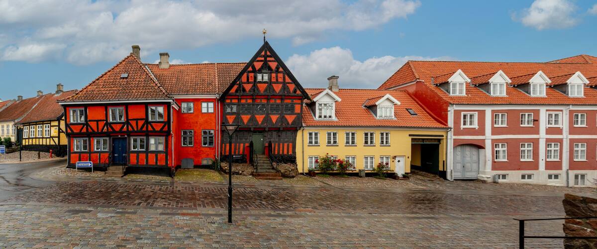 A row of colorful half-timbered houses with red and yellow facades, a cobblestone street, and a clear blue sky.