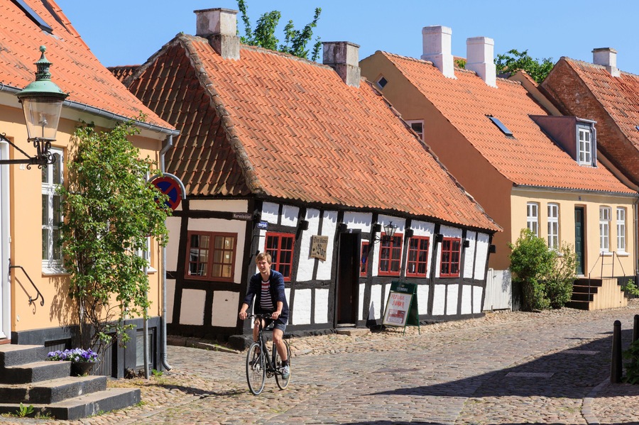 DB1RGY Quaint old Den skaeve bar (The Crooked Bar) with man cycling on cobbles along cobbled street. Overgade Ebeltoft Jutland Denmark