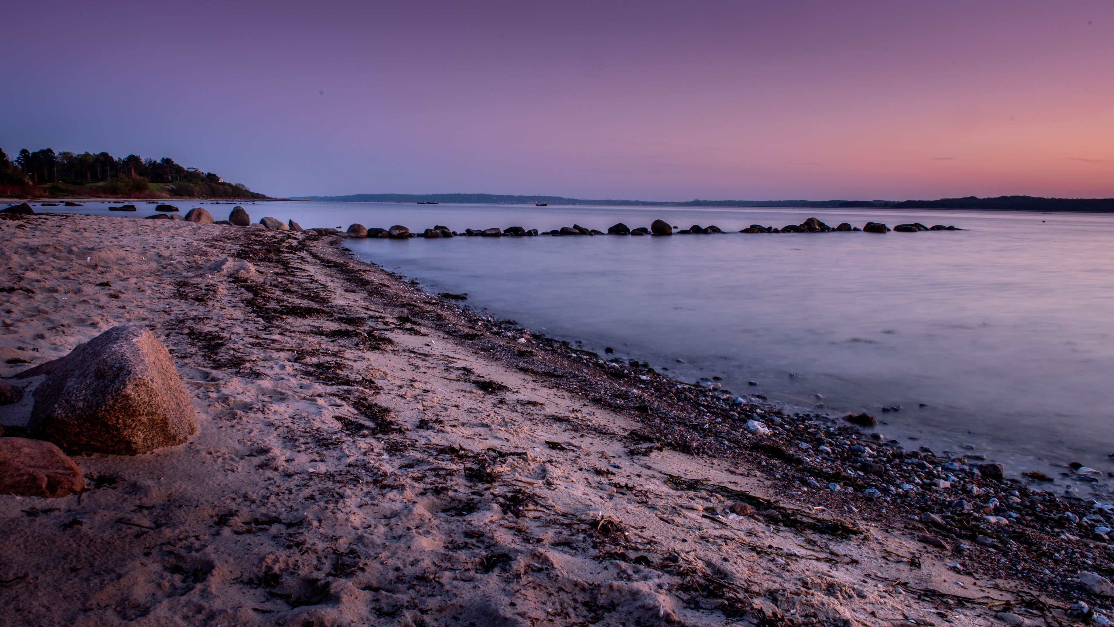 A beach with rocks and calm water at dusk.