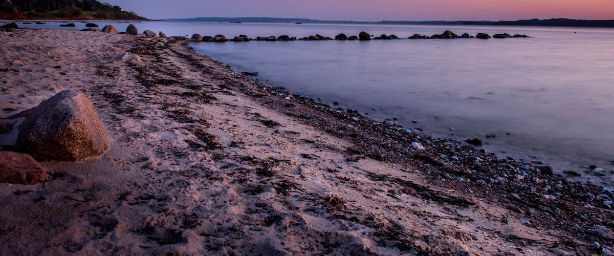 A beach with rocks and calm water at dusk.