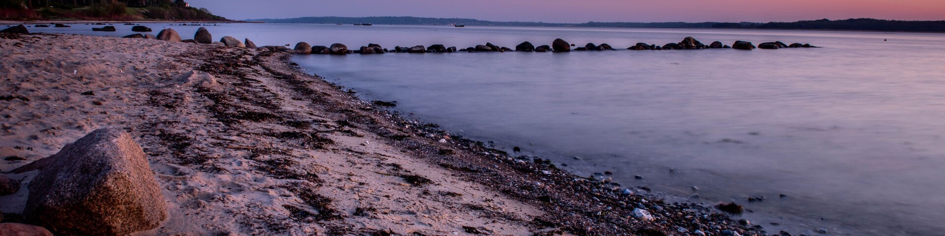 A beach with rocks and calm water at dusk.