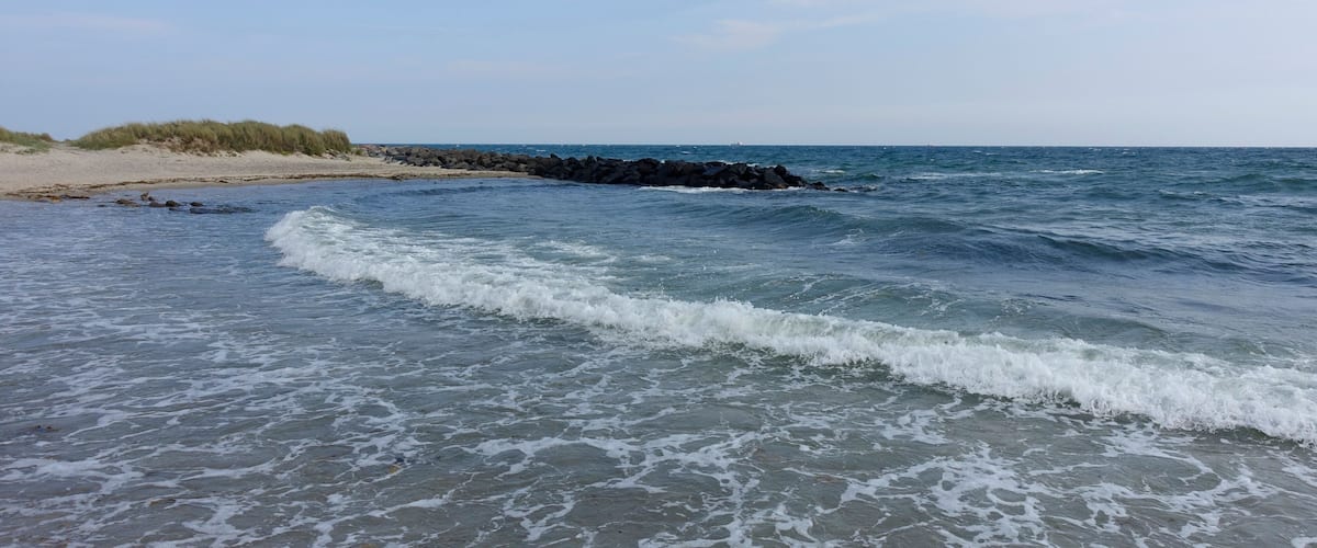 A beach with waves, a sandy shore, and a rocky outcrop in the distance.