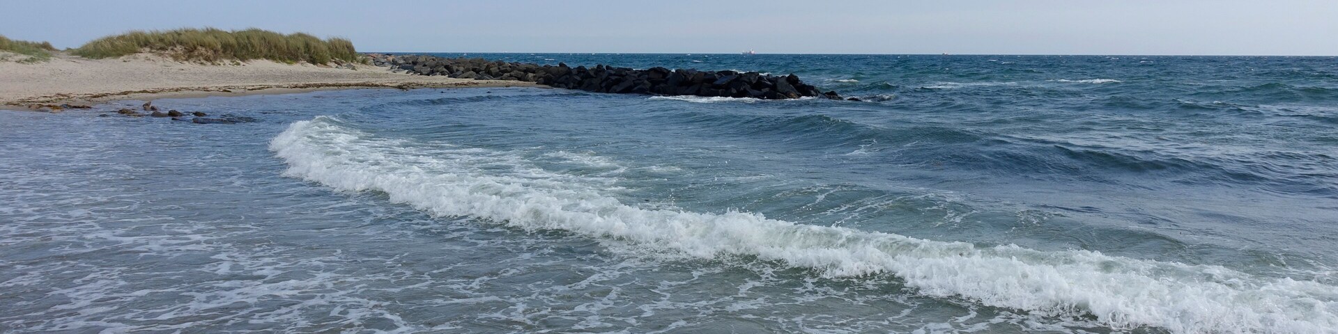 A beach with waves, a sandy shore, and a rocky outcrop in the distance.