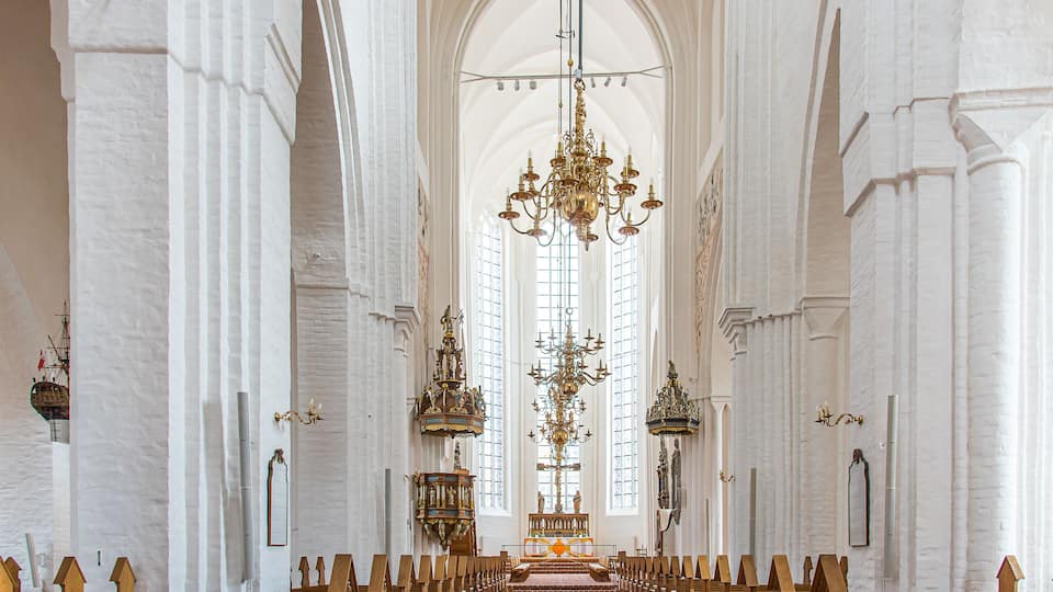 An interior of a church with high arched ceilings, wooden pews, and ornate chandeliers.