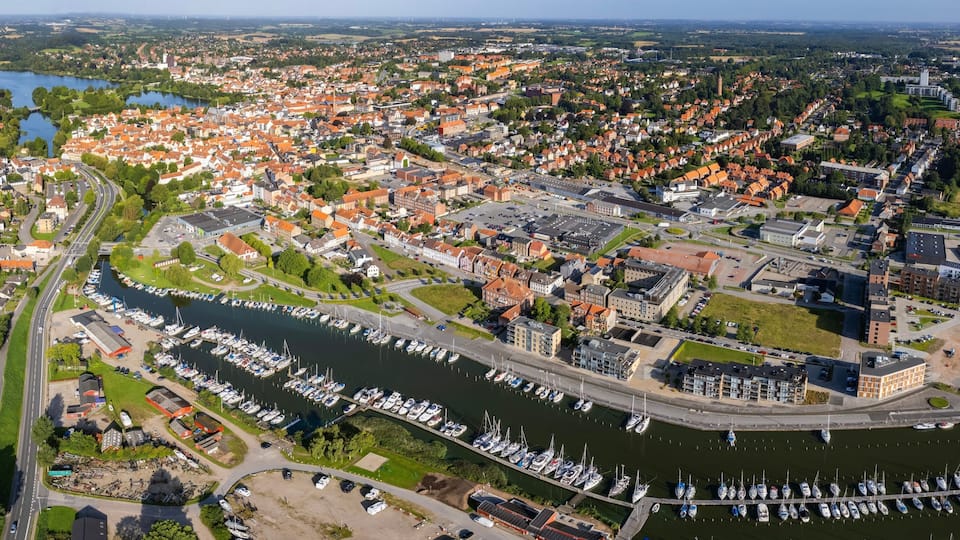 An aerial view of a town with a marina filled with boats, surrounded by residential areas and a river.