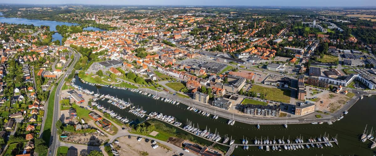An aerial view of a town with a marina filled with boats, surrounded by residential areas and a river.
