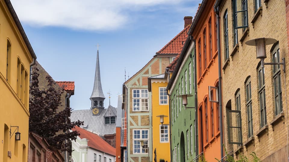A narrow street lined with colorful buildings, a church spire, and a clock tower.