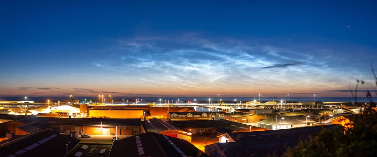A coastal industrial area at dusk with illuminated buildings and a clear sky.
