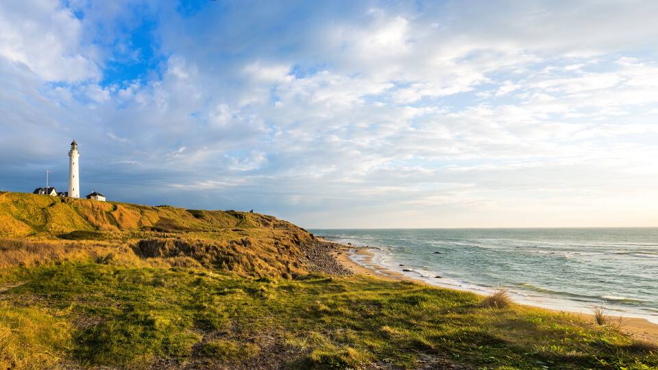 A lighthouse on a grassy cliff overlooking the ocean.