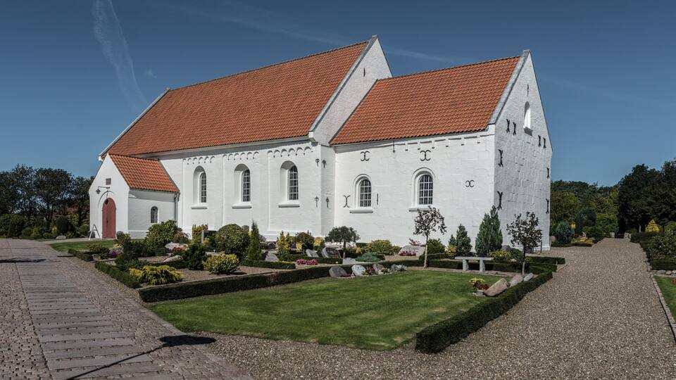 A white building with a red roof, surrounded by a well-maintained garden and a gravel path.