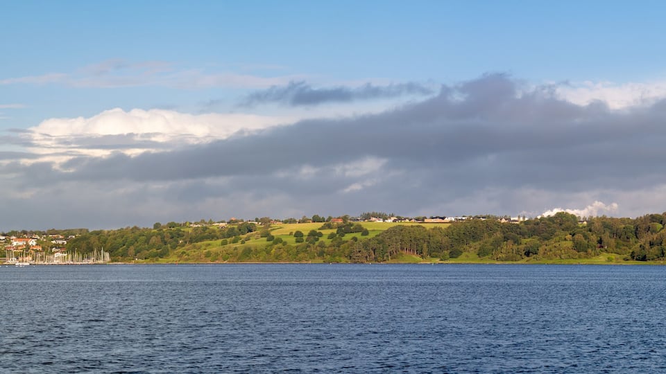 A coastal town with a lighthouse, green hills, and a calm sea.