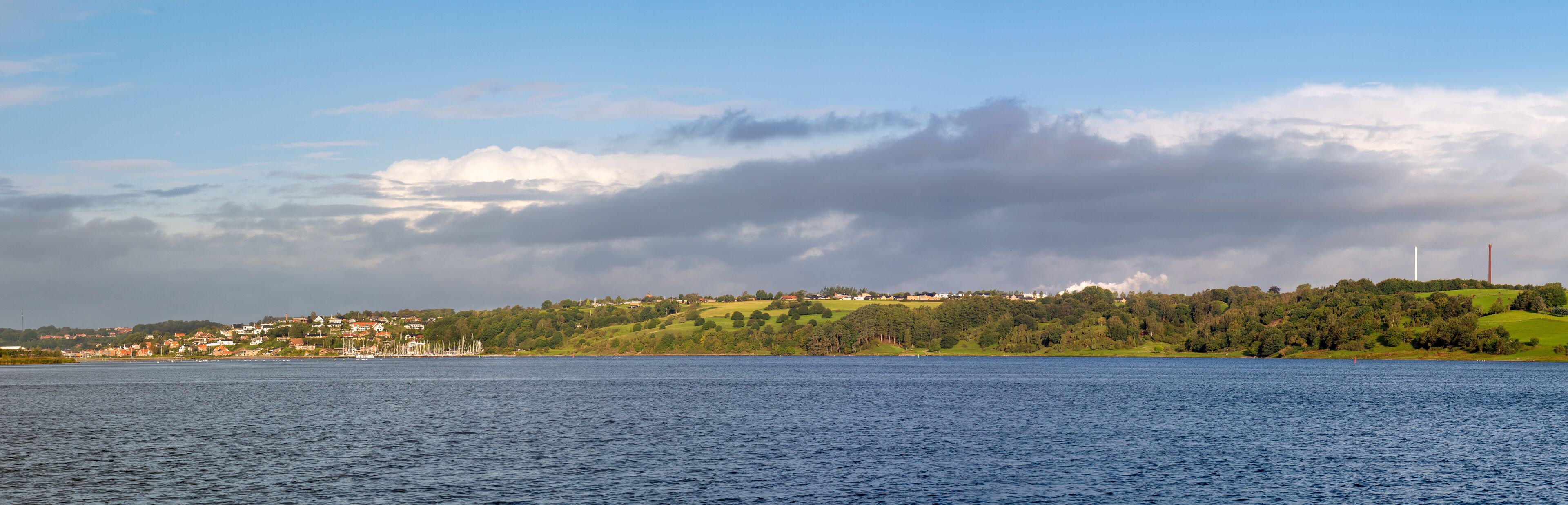 A coastal town with a lighthouse, green hills, and a calm sea.