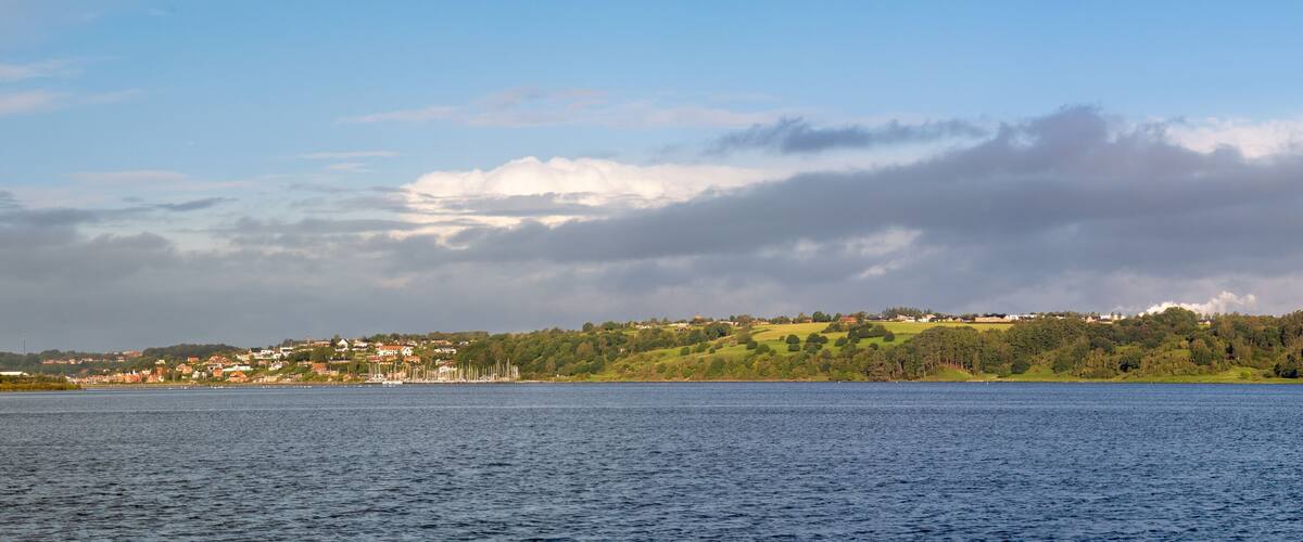 A coastal town with a lighthouse, green hills, and a calm sea.