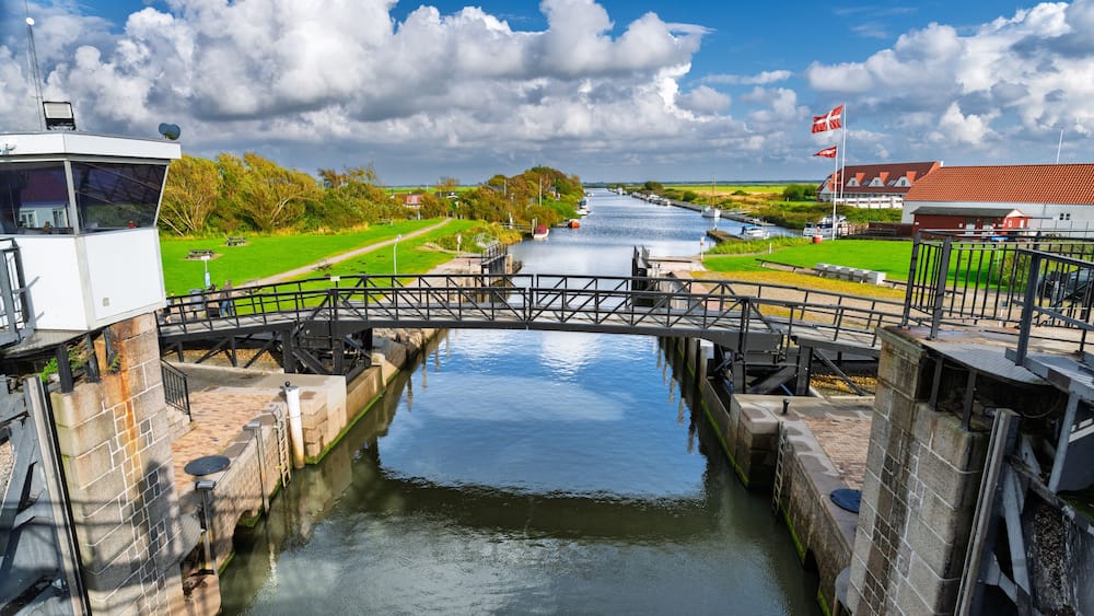 A canal with a lock system, a bridge, and a building with a red roof.