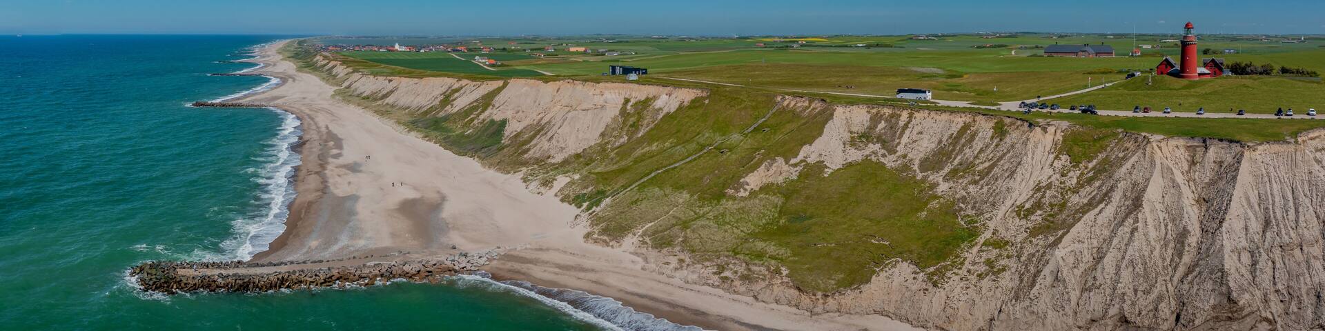 Cliffs and breakwaters on the coast of Bovbjerg Fyr at Ferring near Lemvig. View of the North Sea, lighthouse Bovbjerg Fyr and the village of Ferring with white church and Ferring Sø Fjord.