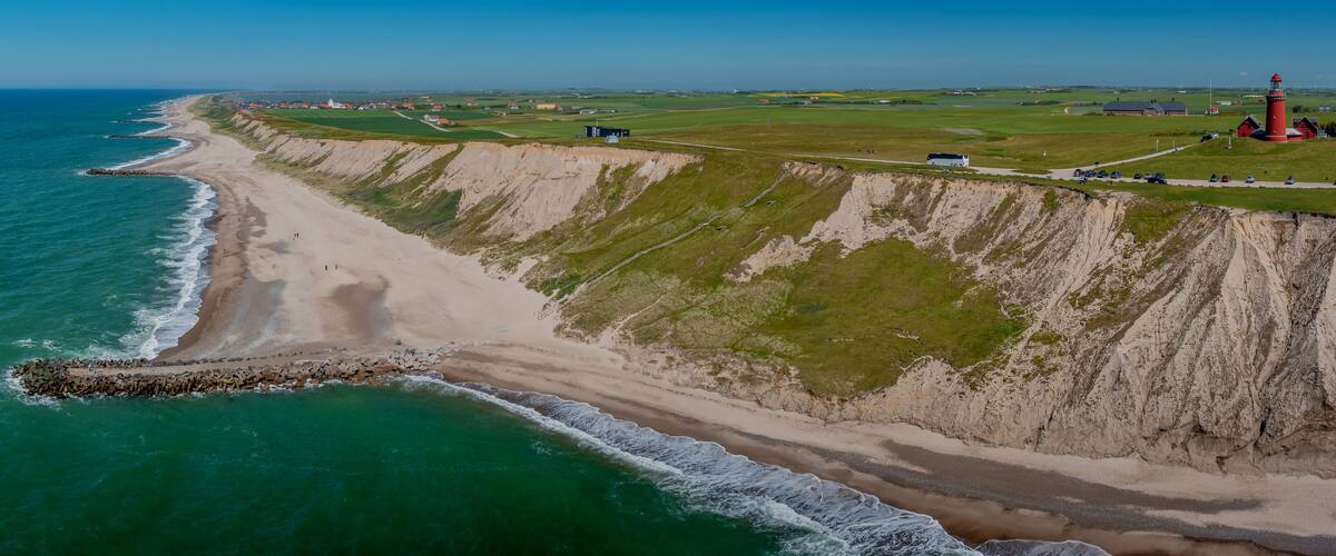A coastal landscape with a beach, cliffs, a lighthouse, and a small settlement.