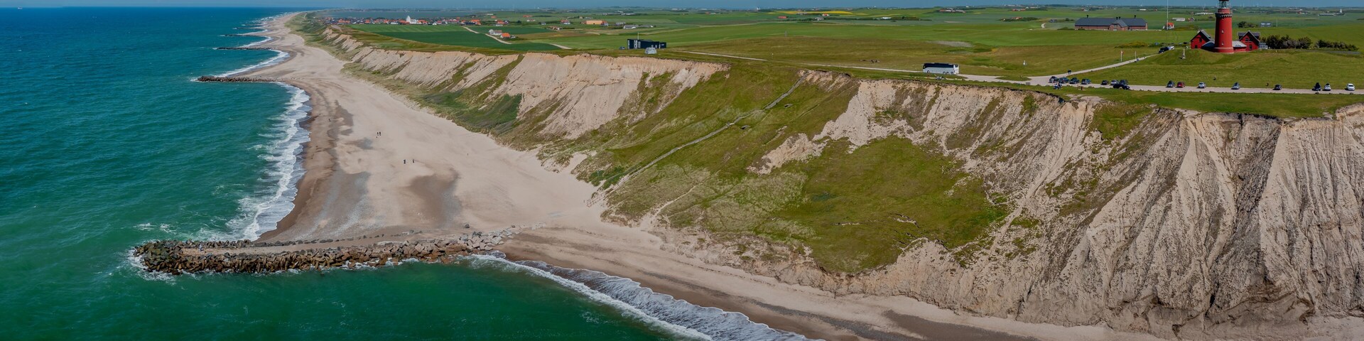 A coastal landscape with a beach, cliffs, a lighthouse, and a small settlement.