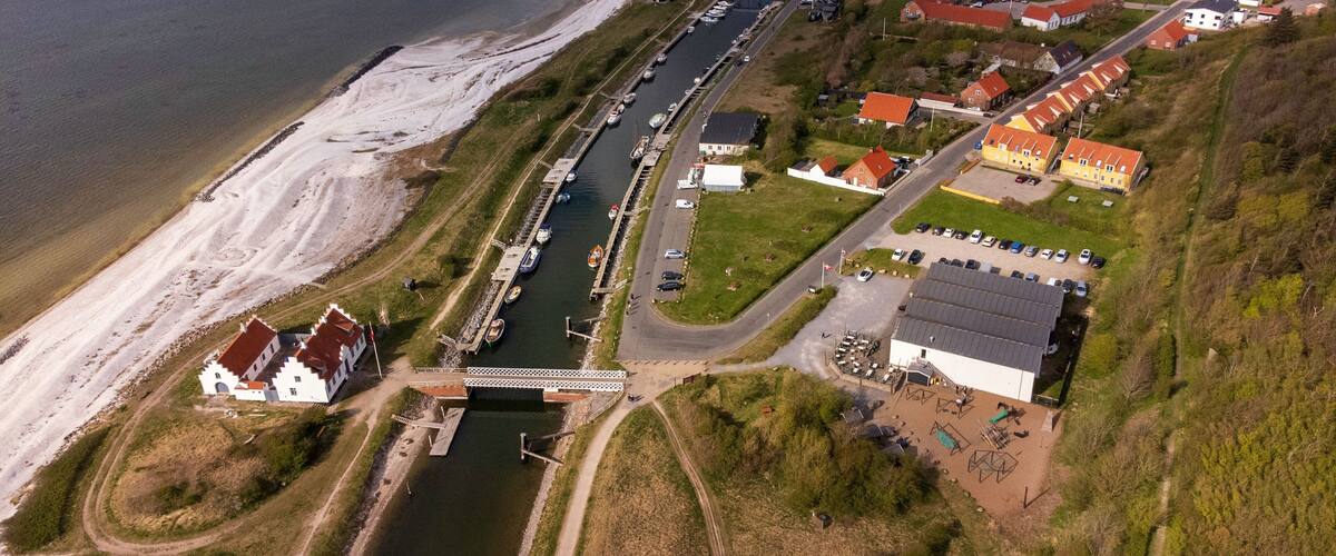 An aerial view of a coastal town with a marina, sandy beach, and residential buildings.