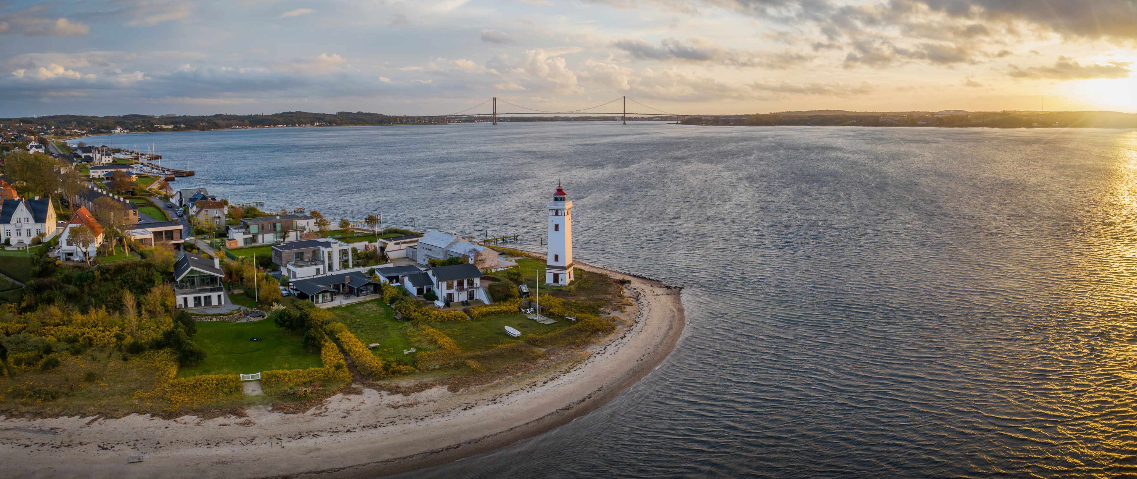 A coastal town with a lighthouse, houses, a bridge, and a beach.