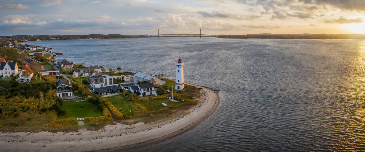 A coastal town with a lighthouse, houses, a bridge, and a beach.