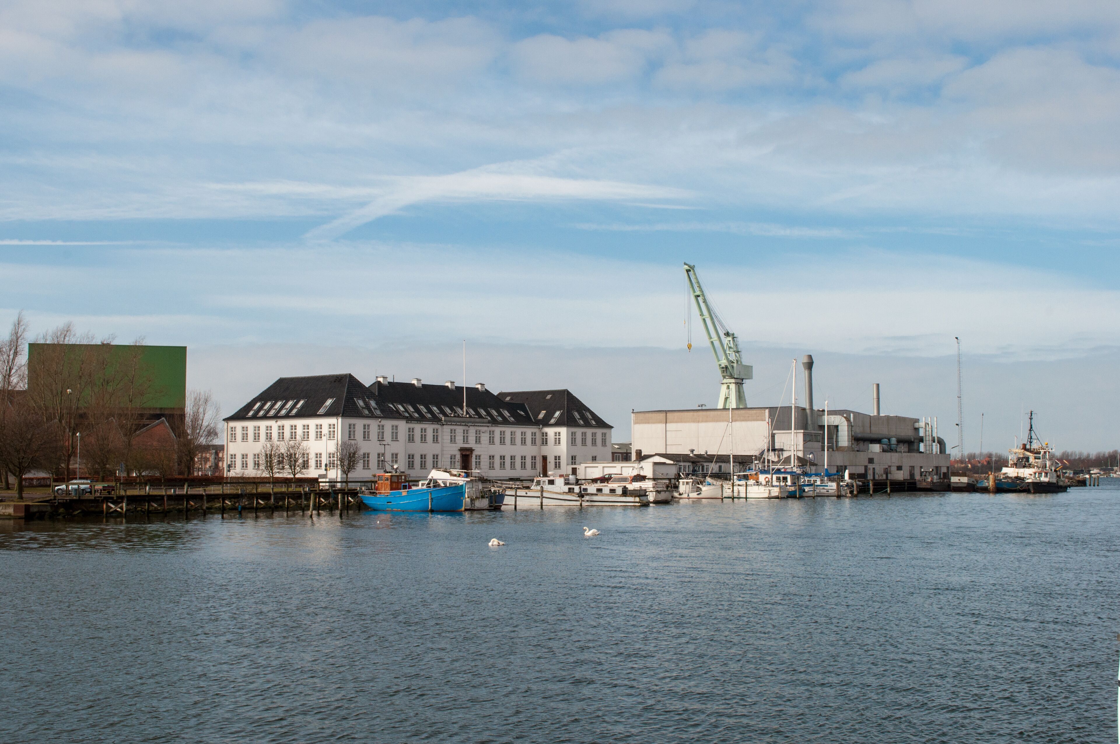 A harbor with a large white building, a blue boat, and a crane.
