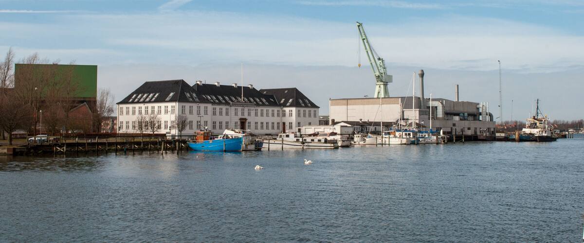 A harbor with a large white building, a blue boat, and a crane.