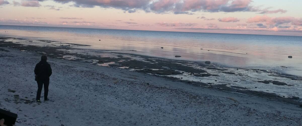 A beach with a person standing on the sand, the ocean, and a sky with clouds.