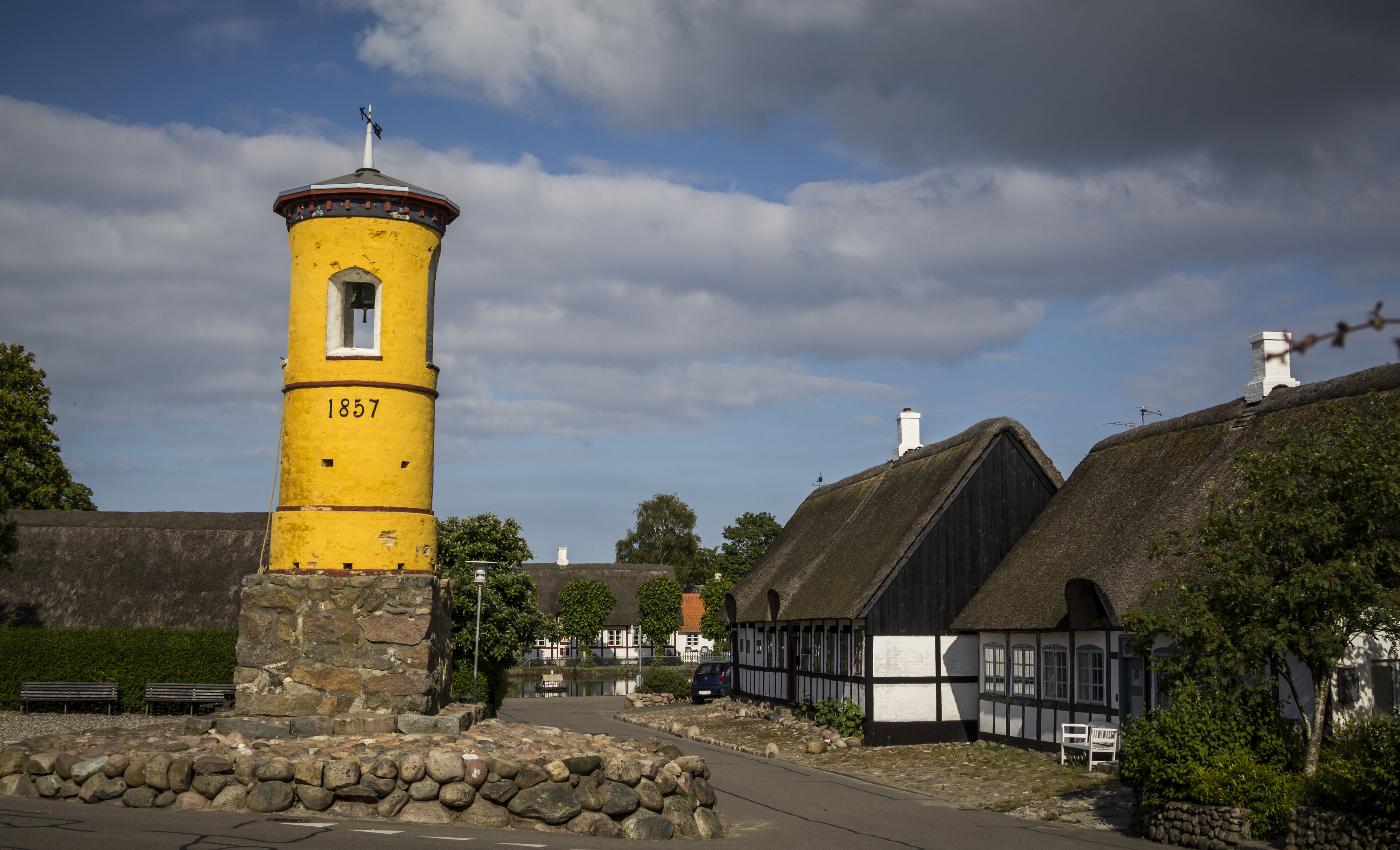 A yellow tower with the number 1857, surrounded by traditional houses and a stone wall.
