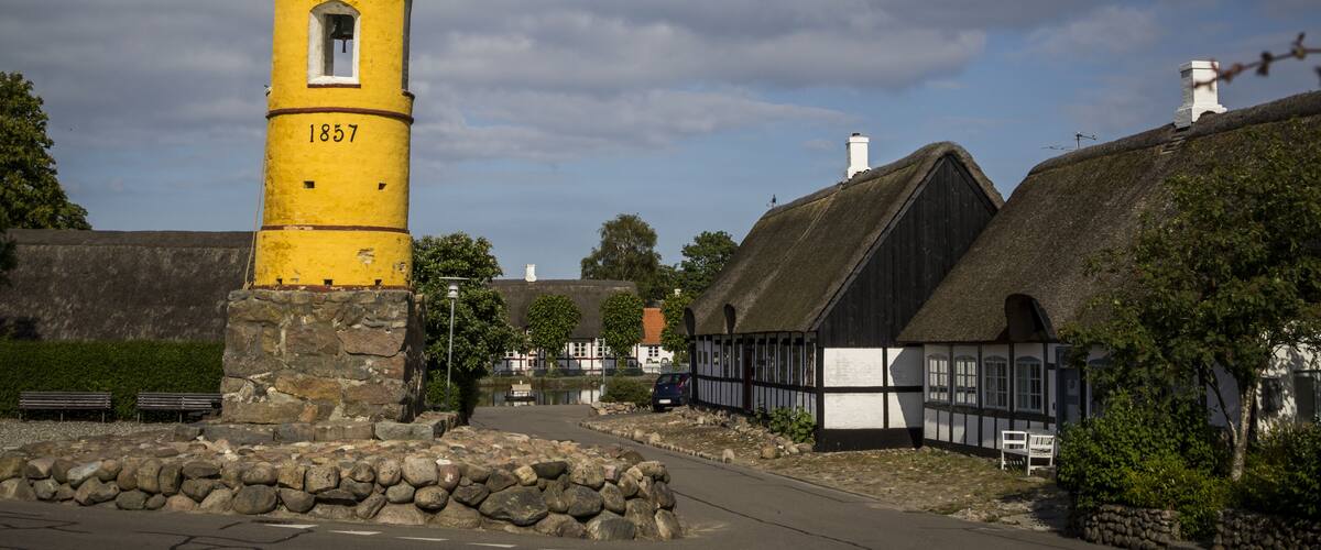 A yellow tower with the number 1857, surrounded by traditional houses and a stone wall.
