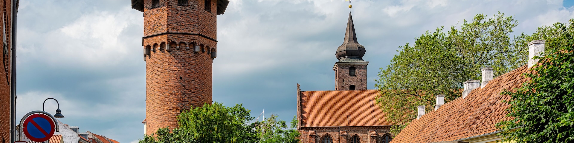 A historic tower with a pointed roof, a church with a dome, and a yellow building with a red gate.