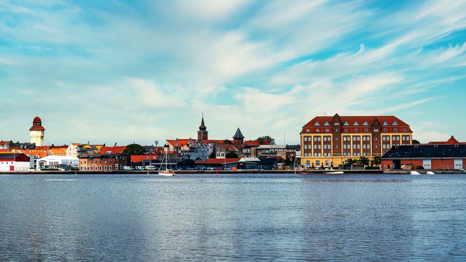 A waterfront cityscape with historic buildings, a prominent church tower, and a large yellow building.