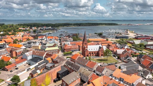 Aerial view of Nykøbing Mors, North Jutland Region, Denmark—harbor cityscape and skyline with red-roofed houses, landmark church, marina, and Limfjord coastline under dramatic summer clouds