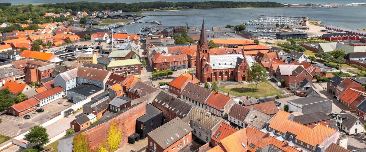 A coastal town with red-roofed buildings, a prominent church, and a marina.