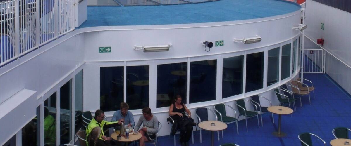 A cruise ship deck with a pool, outdoor seating, and a lifeboat.