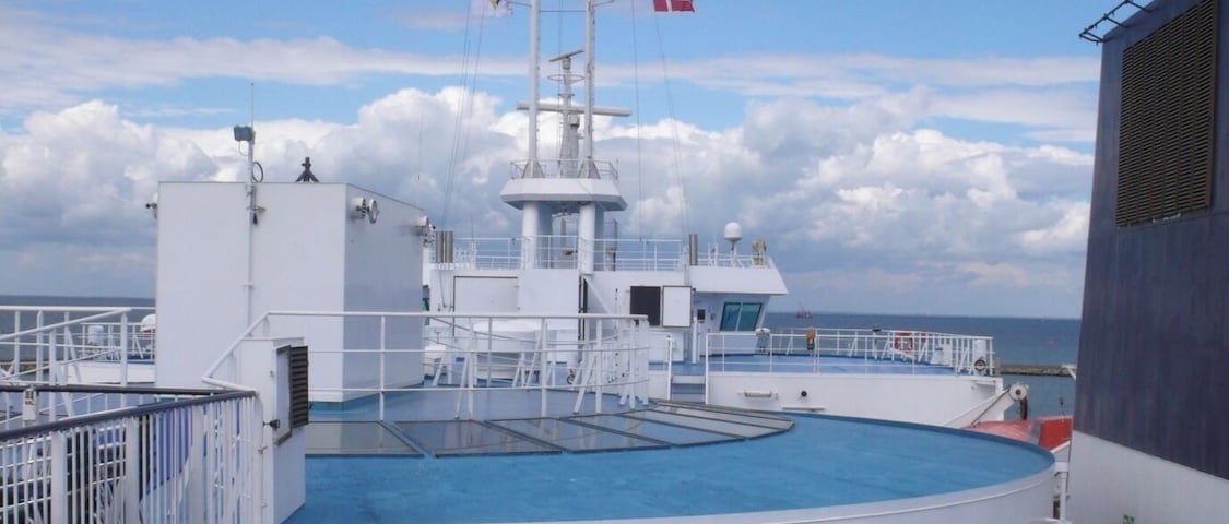 A cruise ship deck with a pool, outdoor seating, and a lifeboat.