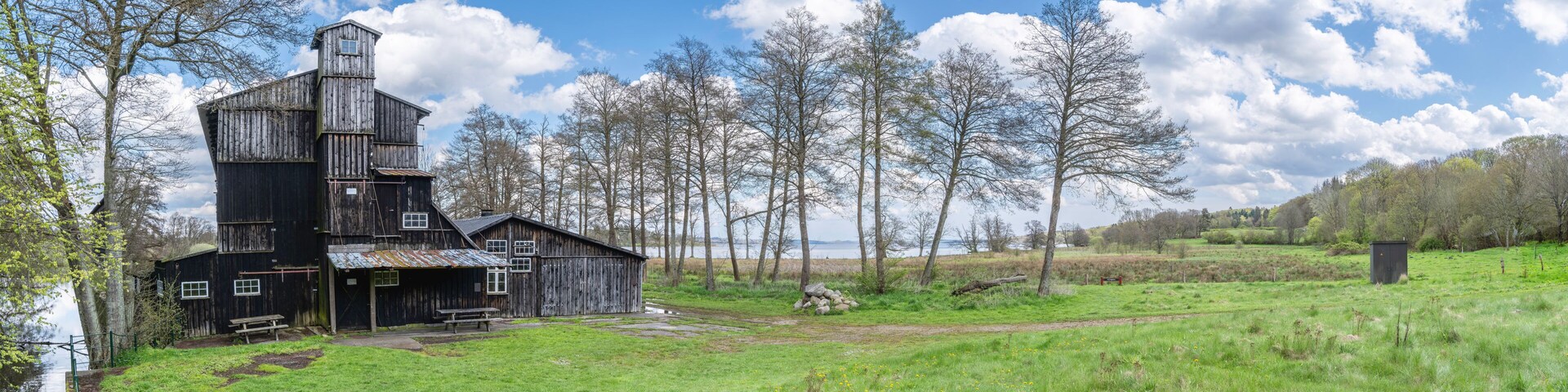 An old wooden barn with a silo, surrounded by a grassy field and trees.