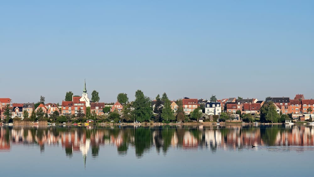 A calm lake reflecting buildings and a church steeple.