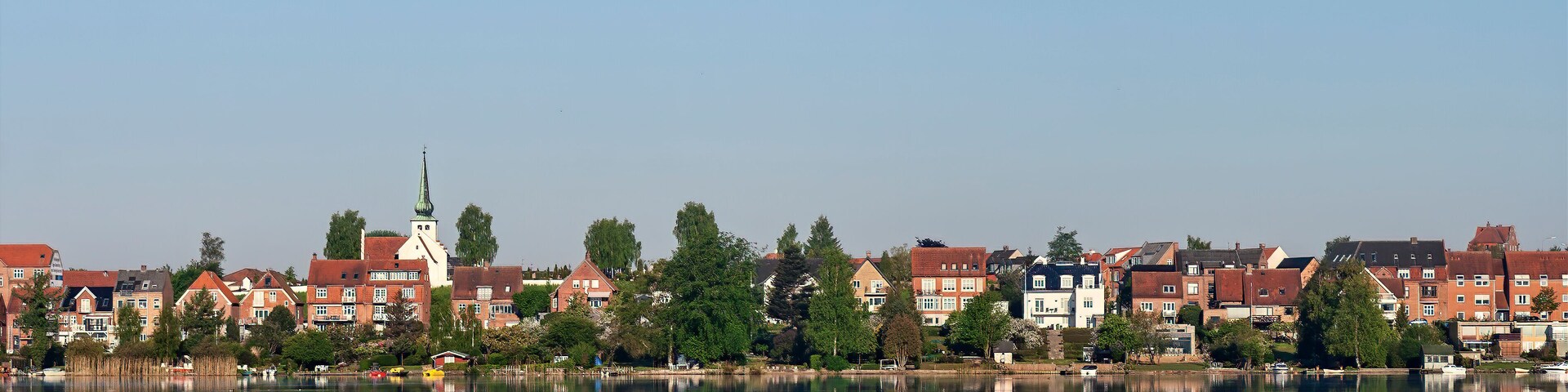 A calm lake reflecting buildings and a church steeple.