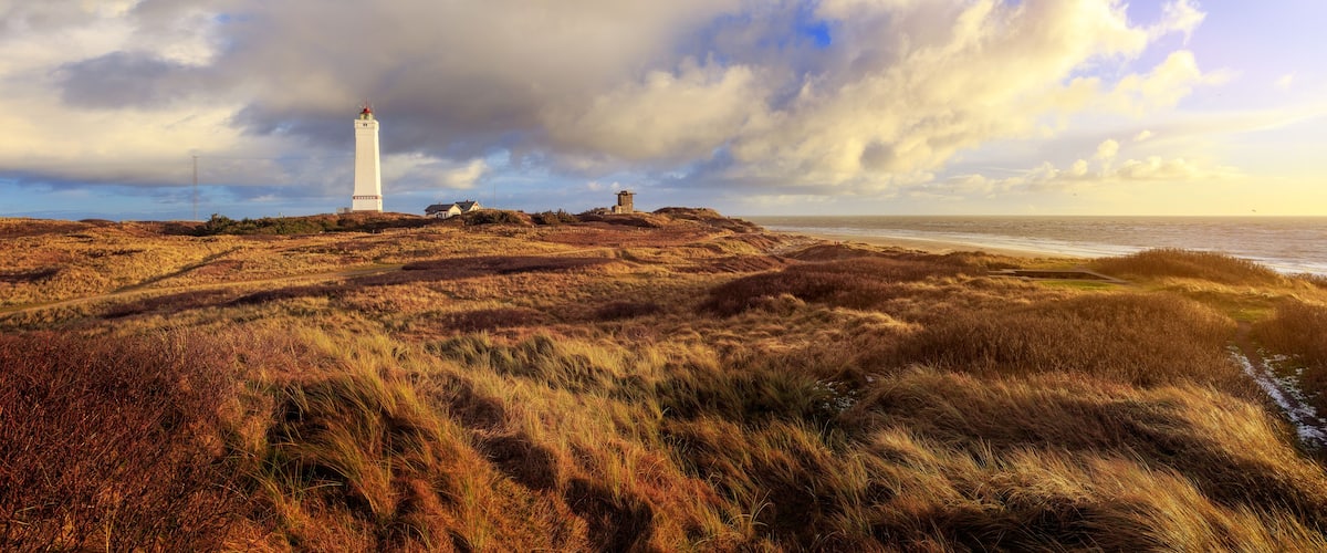 A lighthouse on a grassy hill with a cloudy sky.