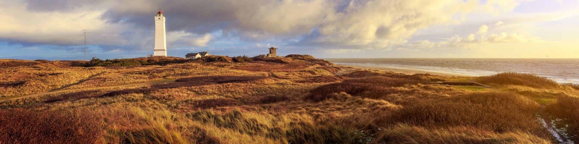 A lighthouse on a grassy hill with a cloudy sky.